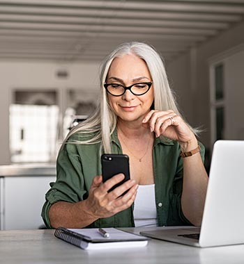 A lady using a smartphone at her laptop computer