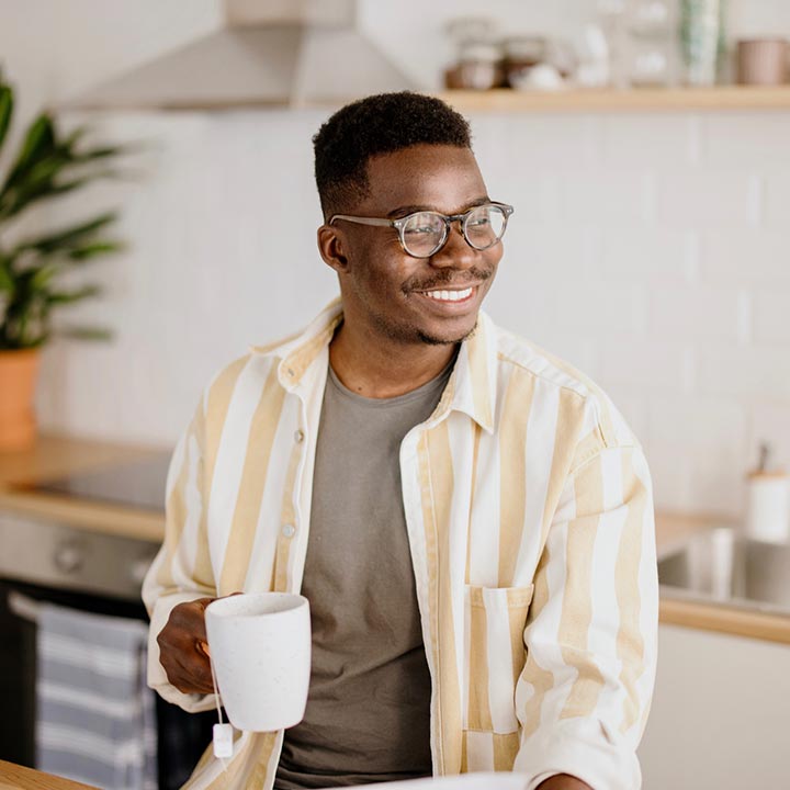 A man smiling and drinking coffee in his kitchen